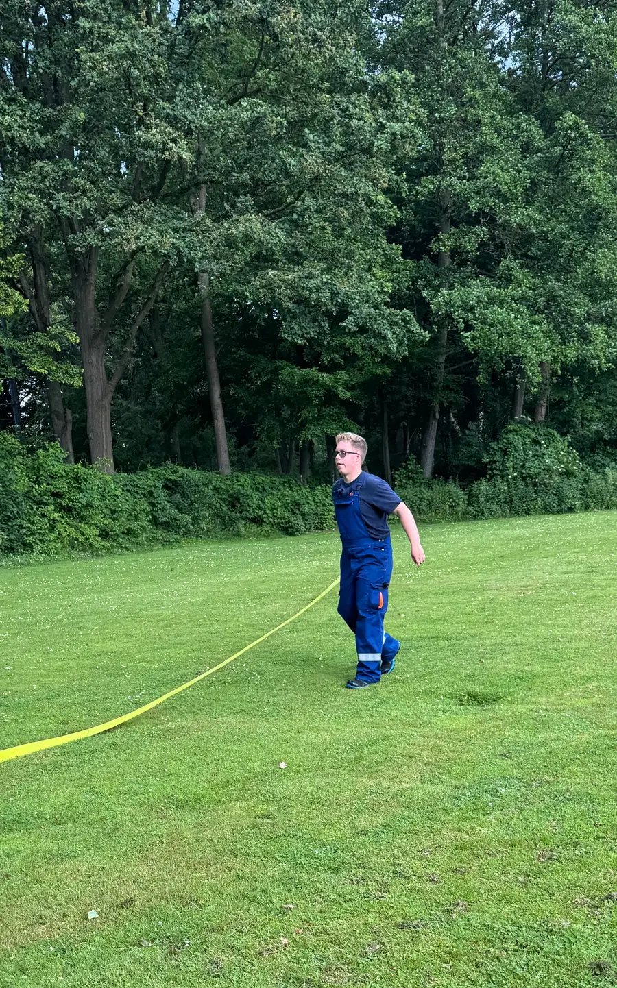 Luca in Einsatzkleidung läuft über eine Wiese, neben ihm ein ausgelegter Schlauch