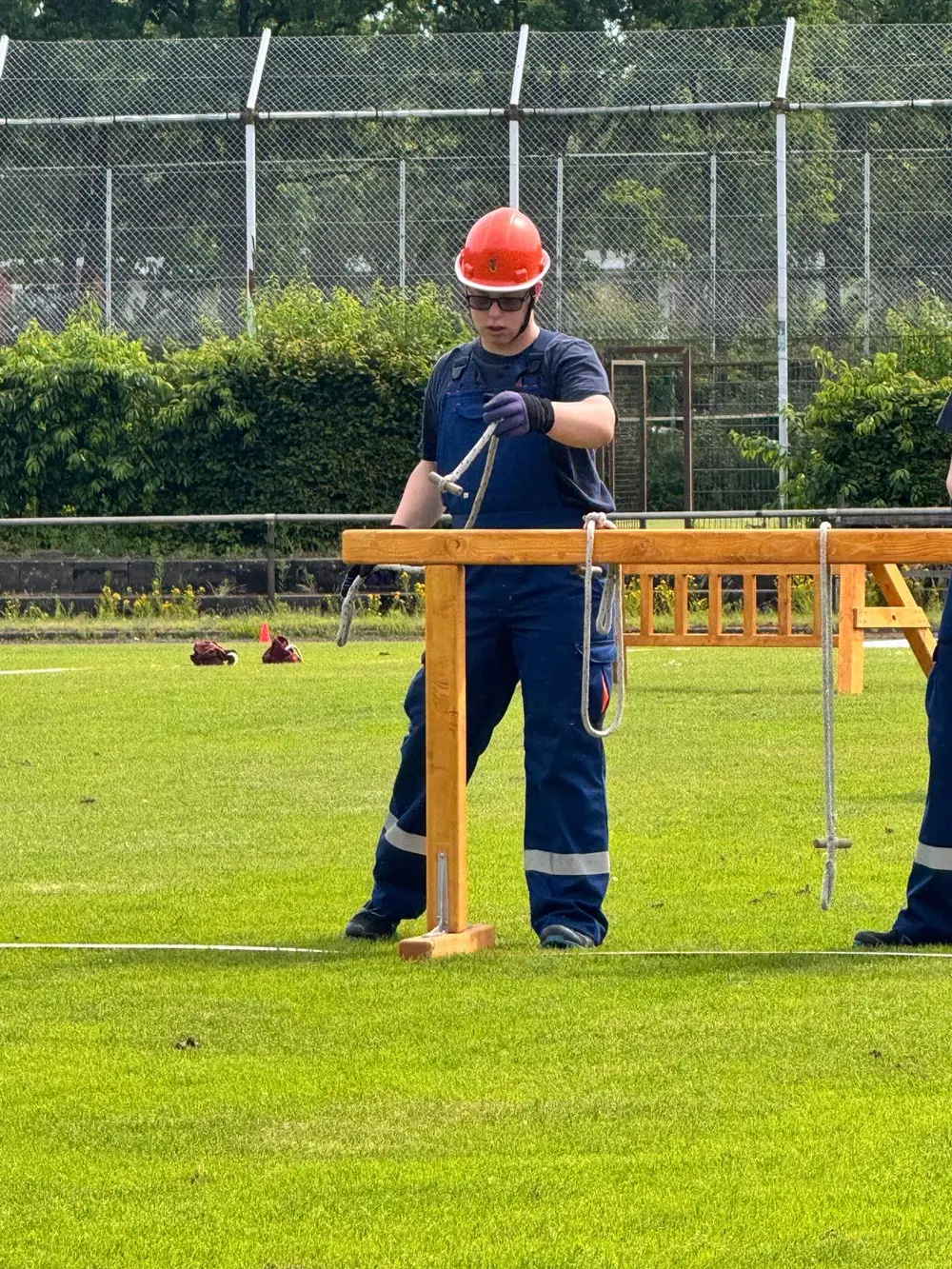 Luca in blauer Einsatzkleidung mit rotem Helm bei einem Wettkampf auf einem Sportplatz